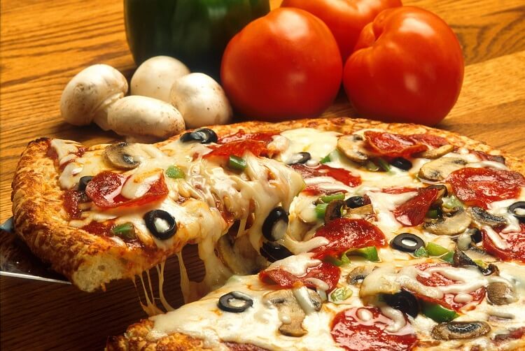 a tasty hot and huge pizza pie with a lot of toppings on it and some vegetables on the side